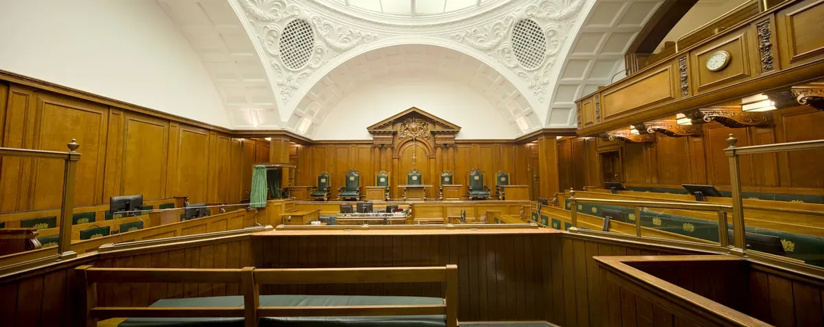 Empty courtroom featuring rich wooden paneling and a decorative ceiling.