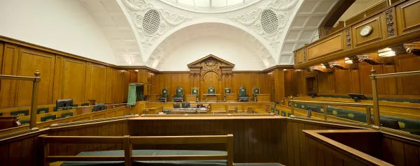 Empty courtroom featuring rich wooden paneling and a decorative ceiling.